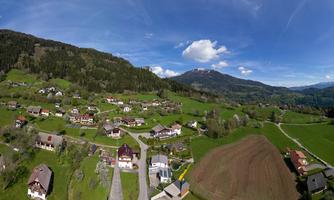 A picturesque landscape with a green valley and scattered houses. In the background, gentle hills and a blue sky can be seen.