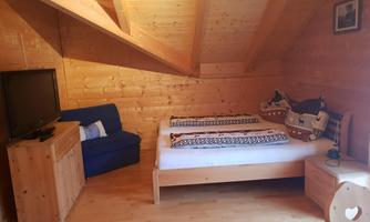 A cozy room with wood paneling and slanted walls. There is a bed, a blue couch, and a television.
