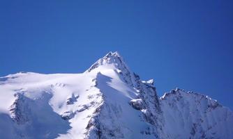 A snow-covered mountain with a clear blue sky in the background. The peak of the mountain is sharp and impressive.