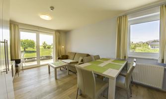 A bright, modern living room with a table and chairs. Large windows provide a view of the garden.