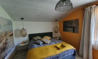 A cozy bedroom with a double bed and a warm color scheme. The walls are partially painted orange and equipped with decorative lamps.