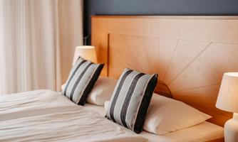 A cozy bedroom with a wooden headboard and two decorative pillows. Soft lighting from the bedside lamps creates a relaxed atmosphere.