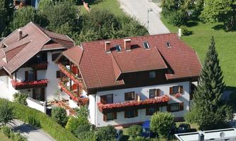 A beautiful house with a red roof and flower boxes. Surrounded by plenty of greenery and trees.