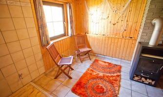 A cozy room with wooden walls and tiled floor. Two chairs and an orange rug create an inviting atmosphere.