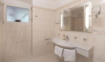 A modern bathroom with a bright tiled floor and a sink. The room features a large mirror and a window.