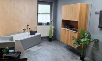 A modern bathroom with a bathtub and a large shower. The walls are in warm colors, and there are plants as well as wooden shelves.
