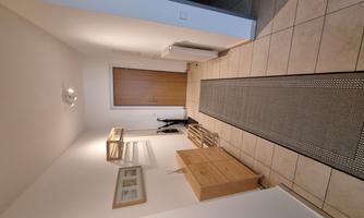 A bright hallway with a long carpet and a wooden box. Pictures are hanging on the wall, and a door leads to another room.