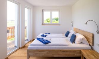 A bright and modern bedroom with two single beds. Large windows provide a view of the outside and ensure plenty of daylight.