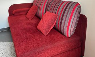 A red sofa with striped cushions. It is positioned against a wall with a modern artwork in the background.