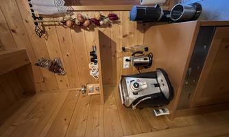 A modern kitchen with wooden walls and wooden shelves. On the countertop are a coffee machine and various kitchen appliances.