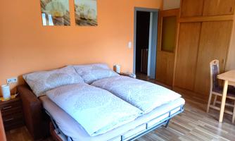 A cozy bedroom with a double bed and orange walls. The room features a wooden floor and a table with chairs.