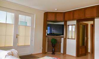 A cozy room with modern furniture and a TV on the wall.  
Large windows provide ample light and an inviting atmosphere.