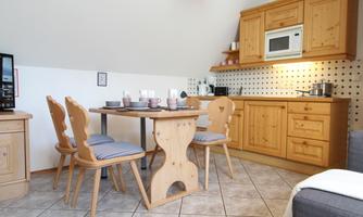A modern kitchen with light wooden cabinets and a dining table. On the table are dishes and some chairs with blue cushions.