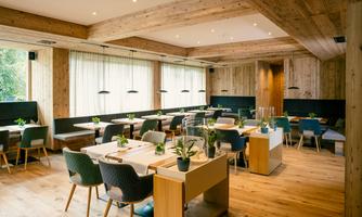A modern restaurant with wooden elements and large windows. The tables are elegantly decorated and there are green plants on the tables.