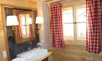 A cozy bathroom with wooden paneling and a large mirror. Red checkered curtains and a modern sink give the room a rustic charm.