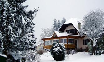A picturesque house surrounded by snow-covered trees and a white winter landscape. The sky is gray and wintry.