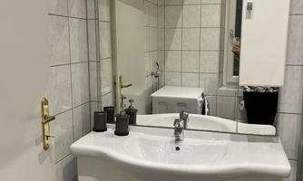 A modern bathroom with a white sink and mirror. The walls are tiled, and there are some decorative elements on the sink.