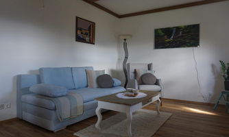 A stylish living room with a blue sofa and an armchair. A wooden table and plants give the space a cozy atmosphere.