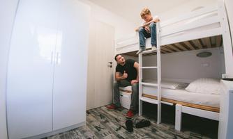 A modern bedroom with a loft bed and a desk. An adult is sitting on a chair while a child is sitting on the ladder to the loft bed.
