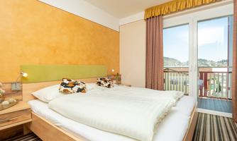 A cozy bedroom with a double bed and soft colors. Large windows offer a view outside and plenty of natural light.