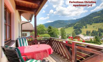 A beautiful balcony with a table and chairs, surrounded by green mountains and a blue sky. Perfect for relaxing hours outdoors.