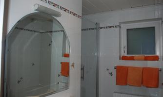 A modern bathroom with a large mirror and a shower. Orange towels are neatly hung.