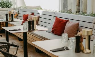 A cozy terrace with a wooden bench and red cushions. There are tables with glasses and elegant accessories.