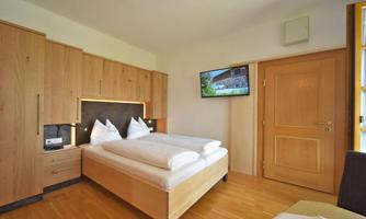 A cozy bedroom with a double bed and two pillows. There is a television on the wall, and the furniture is made of light wood.