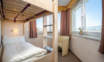A small room with a loft bed and a comfortable armchair. The windows offer a view of the landscape.