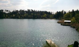 A quiet lake surrounded by trees and meadows. The sun reflects on the water's surface, creating a peaceful atmosphere.