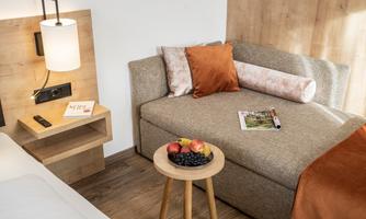 A cozy seating area with a gray sofa and orange decoration. Fresh fruit and a magazine are on a table.