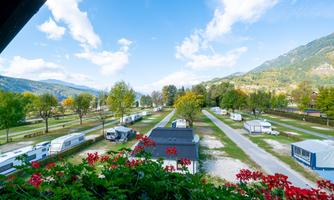 A campsite with caravans in a green landscape. In the background, there are mountains and a blue sky.