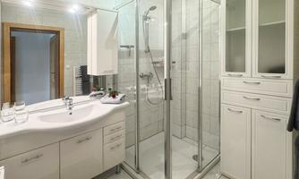 A modern bathroom with a glass shower cabin. There is a bright decor with a sink and a cabinet.