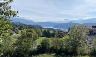 A picturesque landscape with a lake and gentle hills. In the foreground, there are trees and some buildings.