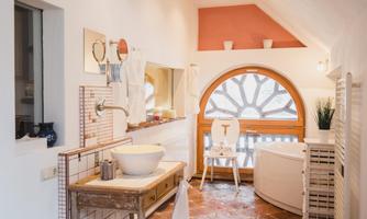 A bright bathroom with a large round window and modern details. On the table is a sink, surrounded by stylish decorations.