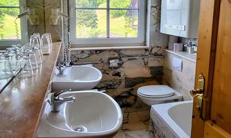 A modern bathroom with two sinks, a bathtub, and a toilet. Large windows let in plenty of daylight and offer a view of nature.