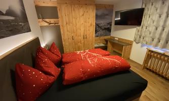 A cozy bedroom with a double bed and red bedspreads. The wooden details and wall art create a warm atmosphere.