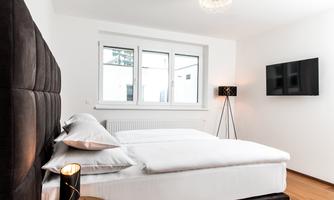 A modern bedroom with a comfortable double bed and a large window. The wall is brightly painted and there is a television on the wall.