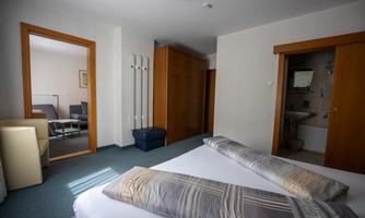 A bright room with a double bed and modern furnishings. Next to the sleeping area, there is another room with a seating area.