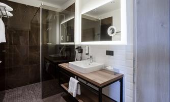 A modern bathroom with a glass shower and a stylish sink. The walls are dark, and a large mirror adds brightness.