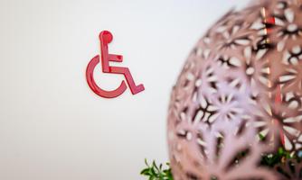 A red sign with the wheelchair symbol on a wall. In the foreground, a decorative lamp with floral patterns is visible.