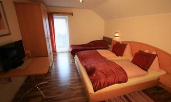 A cozy room with two beds and red bedspreads. There is a desk and a television, as well as windows with natural light.