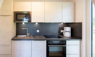 A modern kitchen with a sink, stove, and microwave. The kitchen cabinets are designed in a light and simple style.