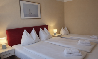 A cozy room with two beds and red pillows. Next to the beds are nightstands with lamps.