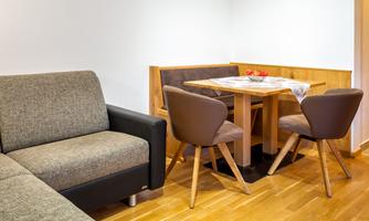 A modern living room with a gray sofa and a wooden table. The dining area is decorated with beige chairs and fresh fruits.
