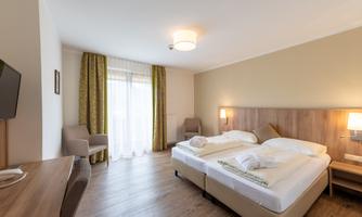 A modern hotel room with two beds and a desk. Large windows let in plenty of light and the decor is bright and welcoming.