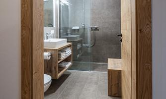 A modern bathroom with a glass enclosure and wooden shelves. The room has a bright, inviting atmosphere.