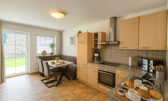 A modern kitchen with bright wooden cabinets and a dining area. On the table, there is a delicious breakfast with rolls, jam, and coffee.