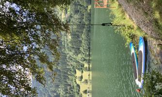 A calm lake with clear water and a picturesque landscape. Two stand-up paddle boards lie at the shore.