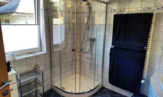 A modern bathroom with a glass shower. The walls are tiled and there is a black towel holder.